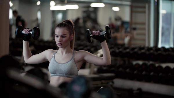 A young girl or woman with dumbbells, doing workout in a gym. Slow motion.