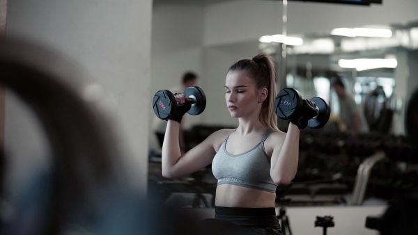 A young girl or woman with dumbbells, doing workout in a gym. Slow motion.