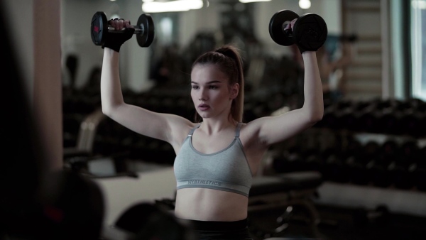 A young girl or woman with dumbbells, doing workout in a gym. Slow motion.