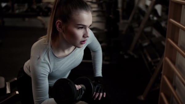 A young girl or woman with dumbbells, doing workout in a gym.