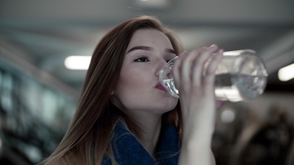 A close-up of young girl or woman in a gym, drinking water from a bottle. Slow motion.