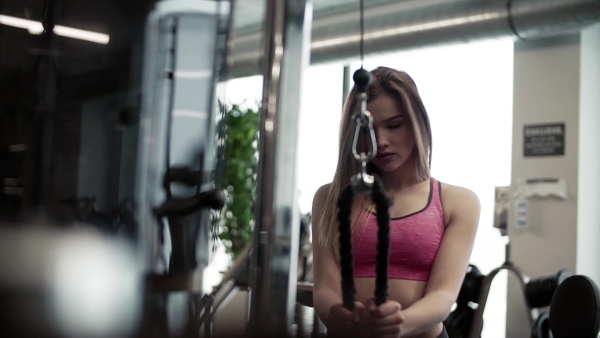 A beautiful young girl or woman doing strength workout in a gym. Slow motion.