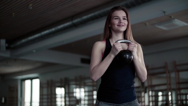 A portrait of a beautiful young girl or woman doing exercise with a kettlebell in a gym. Slow motion.