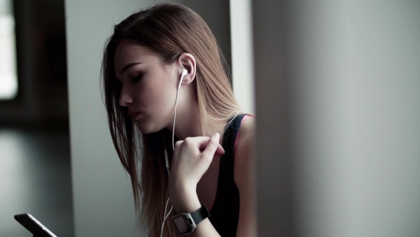 A young girl or woman with earphones, smartphone and smartwatch in a gym. Slow motion.