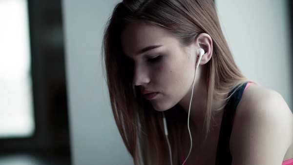 A portrait of sad young girl or woman with earphones in a gym. Slow motion.