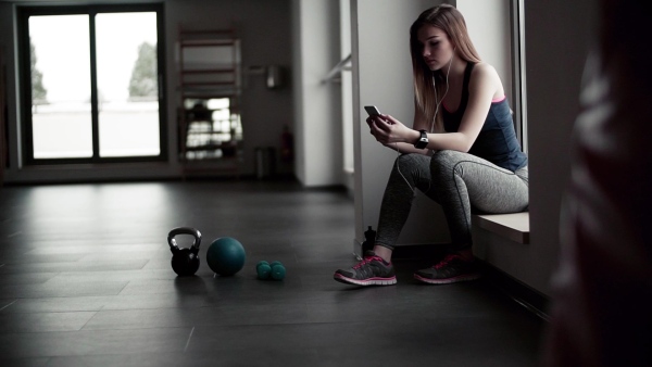 A young girl or woman with earphones, smartphone and smartwatch in a gym. Slow motion.