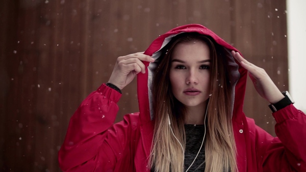 A portrait of beautiful young girl or woman with earphones outdoors in winter, listening to music. Slow motion.