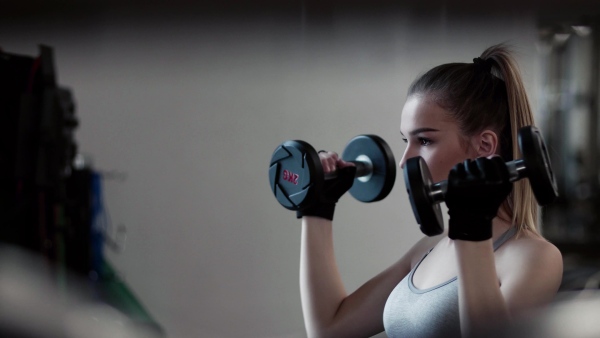 A young girl or woman with dumbbells, doing workout in a gym.