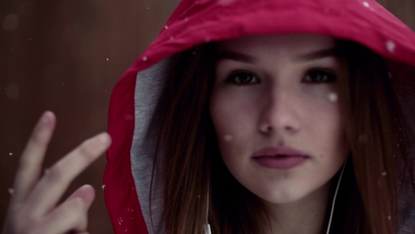 A close-up portrait of beautiful young girl or woman with earphones outdoors in winter, listening to music. Slow motion.