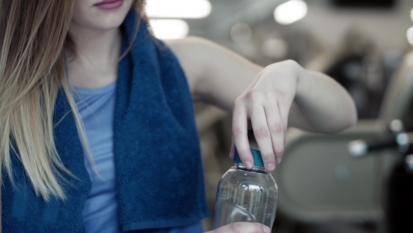 A close-up of young girl or woman in a gym, drinking water from a bottle.