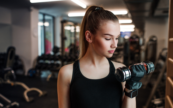 A young girl or woman with dumbbells, doing workout in a gym.