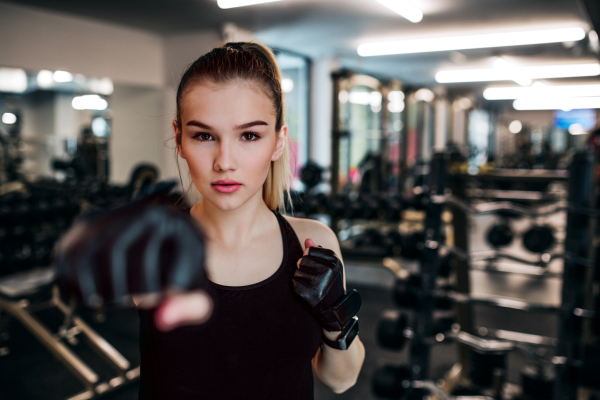 A front view of young girl or woman with gloves, doing exercise in a gym.