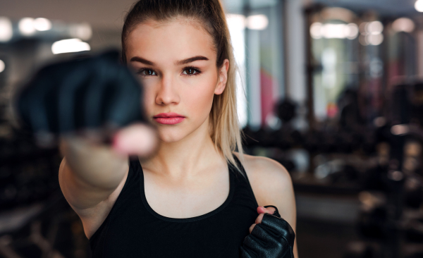 A front view of young girl or woman with gloves, doing exercise in a gym.