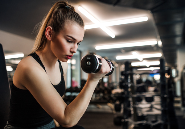 A young girl or woman with dumbbells, doing workout in a gym.