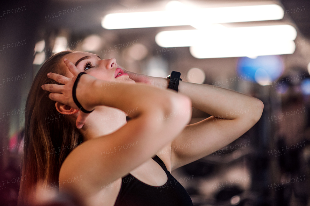 A portrait of a beautiful young girl or woman standing in a gym, making a pony tail.