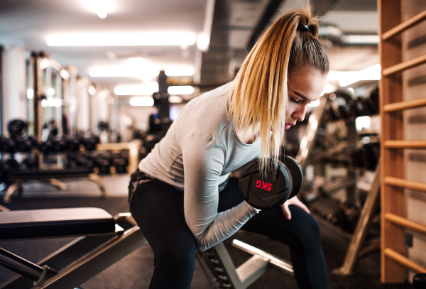 A young girl or woman with dumbbells, doing workout in a gym.