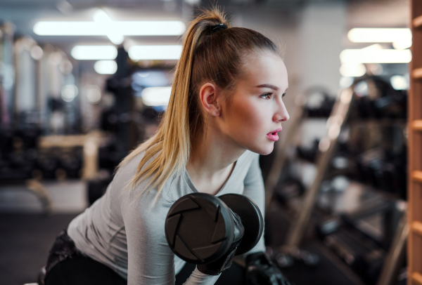 A young girl or woman with dumbbells, doing workout in a gym.