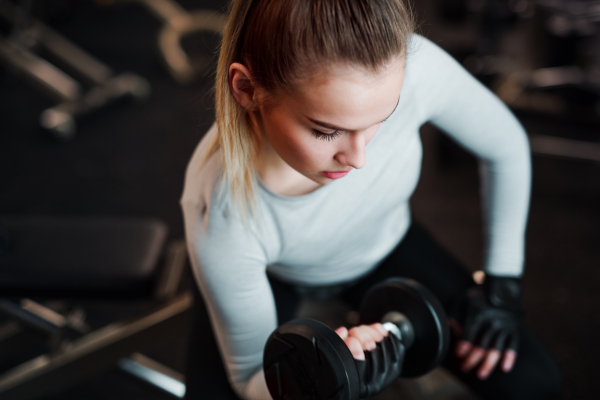 A young girl or woman with dumbbells, doing workout in a gym.