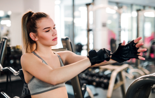 Young girl or woman putting on fingerless gloves in gym.