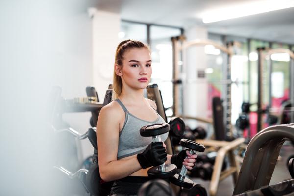 A young girl or woman with dumbbells, doing workout in a gym.