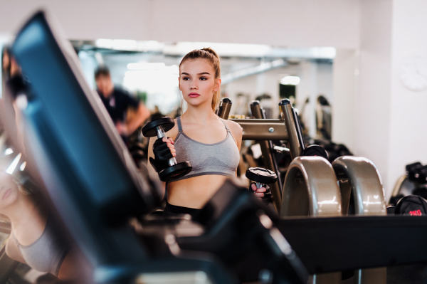 A young girl or woman with dumbbells, doing workout in a gym.