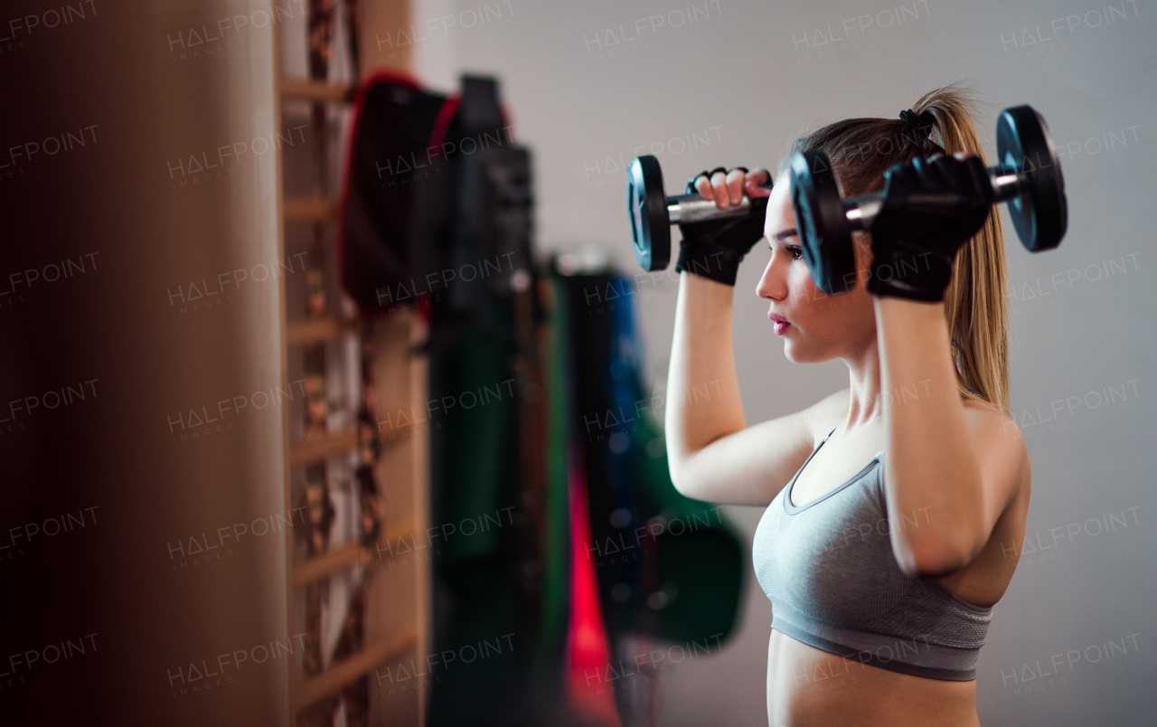 A young girl or woman with dumbbells, doing workout in a gym.