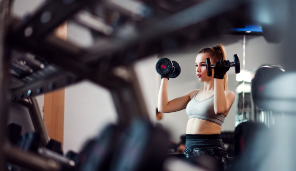 A young girl or woman with dumbbells, doing workout in a gym.