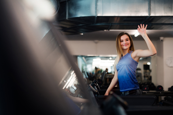 A portrait of a beautiful young girl or woman waving at somebody when doing cardio workout in a gym.