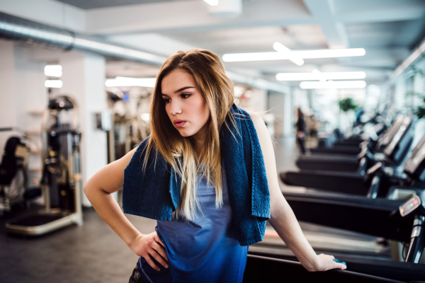 A portrait of young girl or woman with towel around neck standing in a gym.