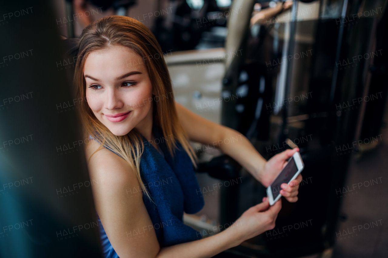 A portrait of happy young girl or woman in a gym, using smartphone.