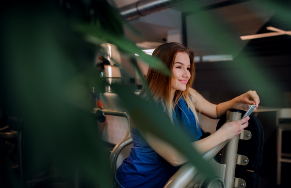 A portrait of happy young girl or woman in a gym, using smartphone.