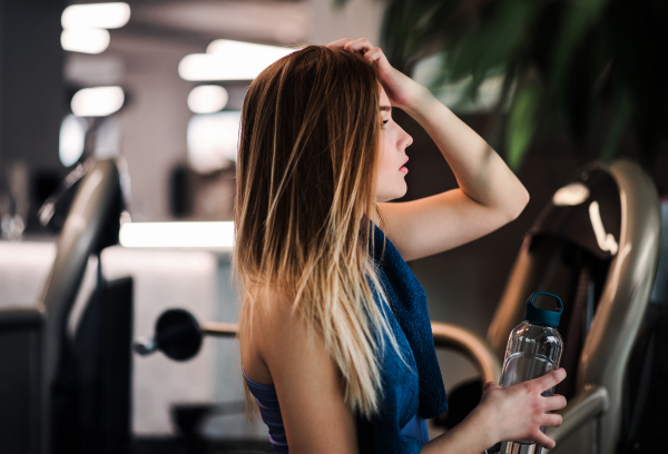 A side view portrait of young girl or woman with water bottle standing in a gym.