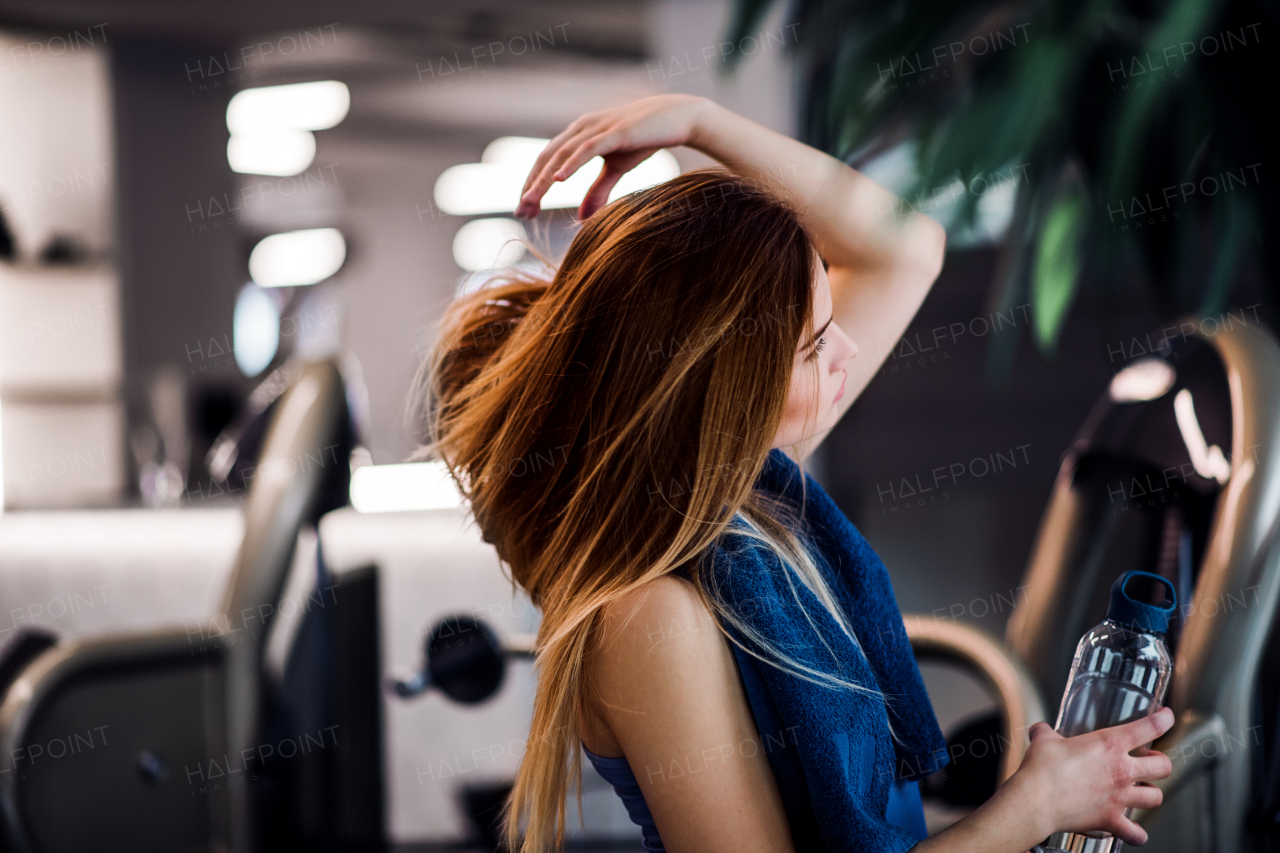 A side view portrait of young girl or woman with water bottle standing in a gym.