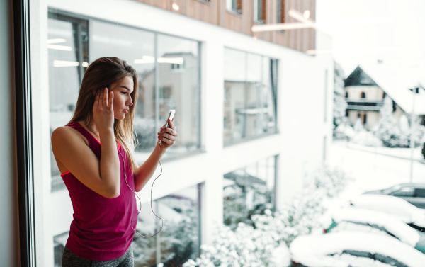 A portrait of a beautiful young girl or woman with earphones and smartphone outside a gym.