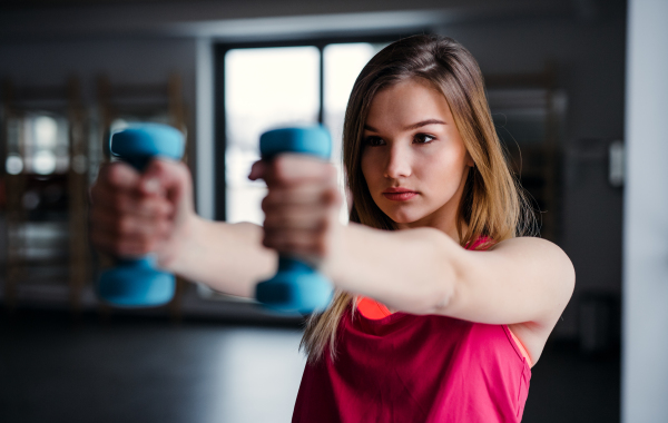 A portrait of a beautiful young girl or woman doing exercise with a dumbbells in a gym.