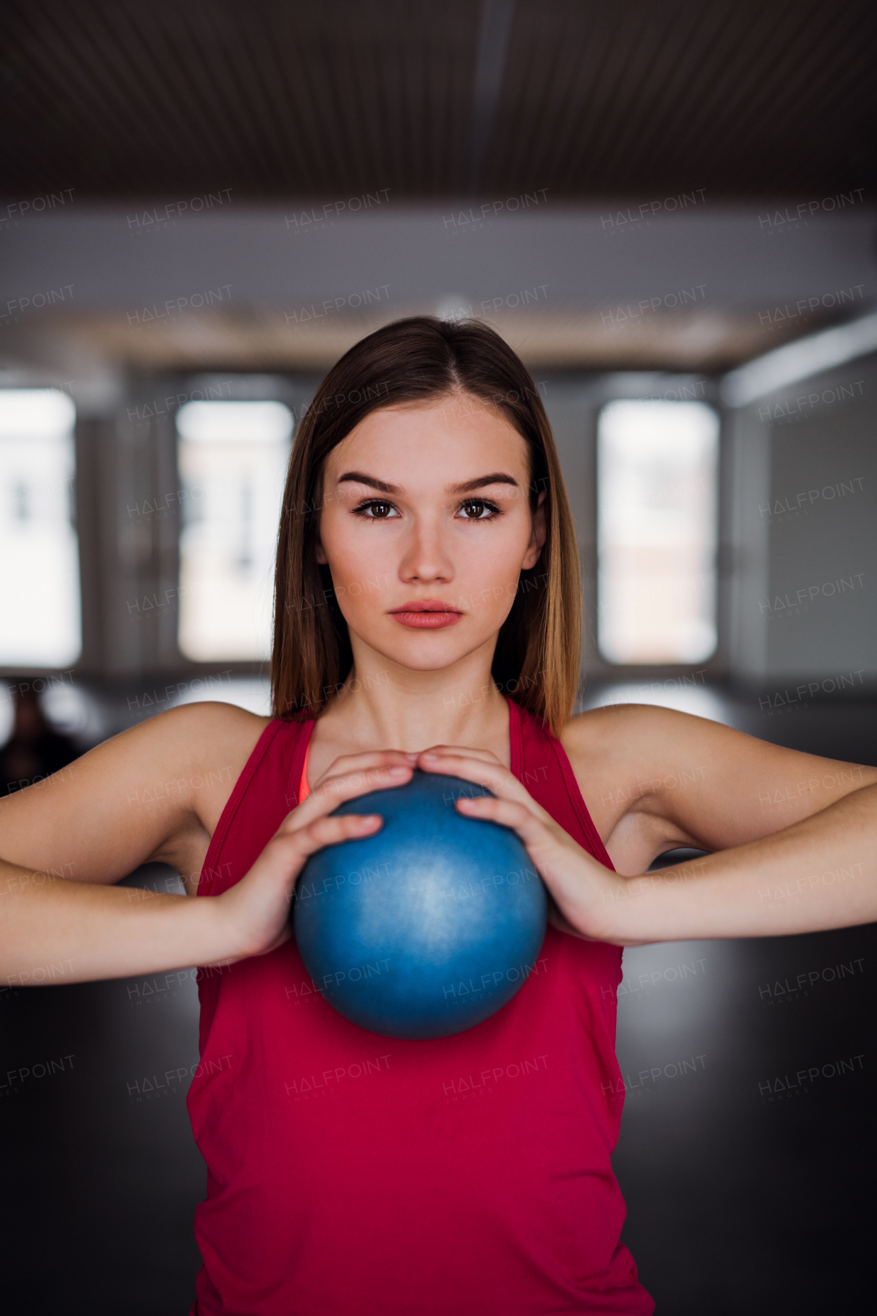 A portrait of a beautiful young girl or woman doing exercise with a ball in a gym.