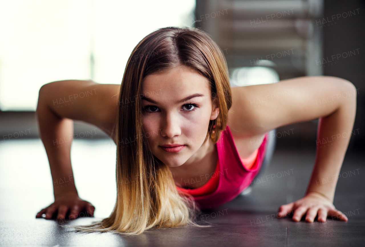 A portrait of a beautiful young girl or woman doing push-ups in a gym.