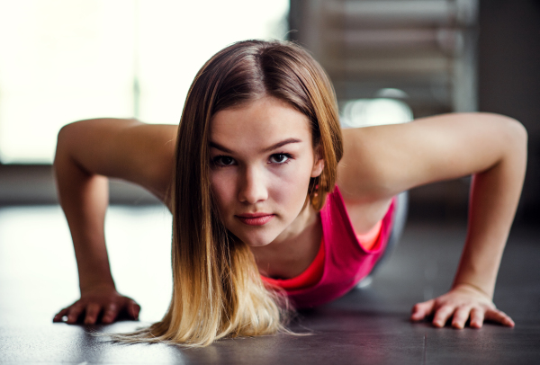 A portrait of a beautiful young girl or woman doing push-ups in a gym.