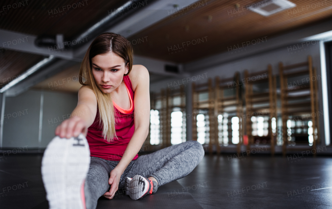 A portrait of a beautiful young girl or woman doing exercise in a gym, stretching.