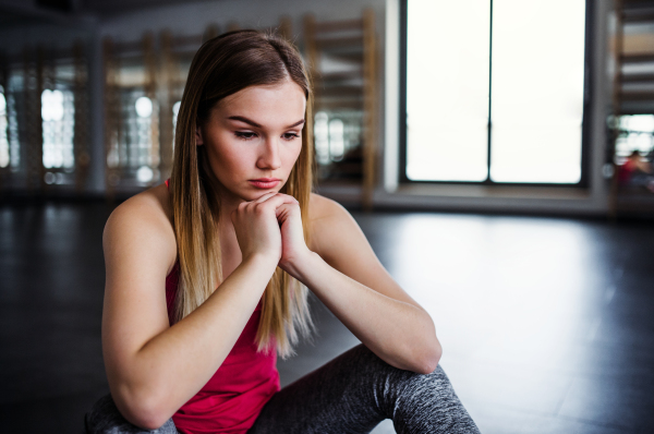 A portrait of young sad and frustrated girl or woman sitting in a gym. Copy space.