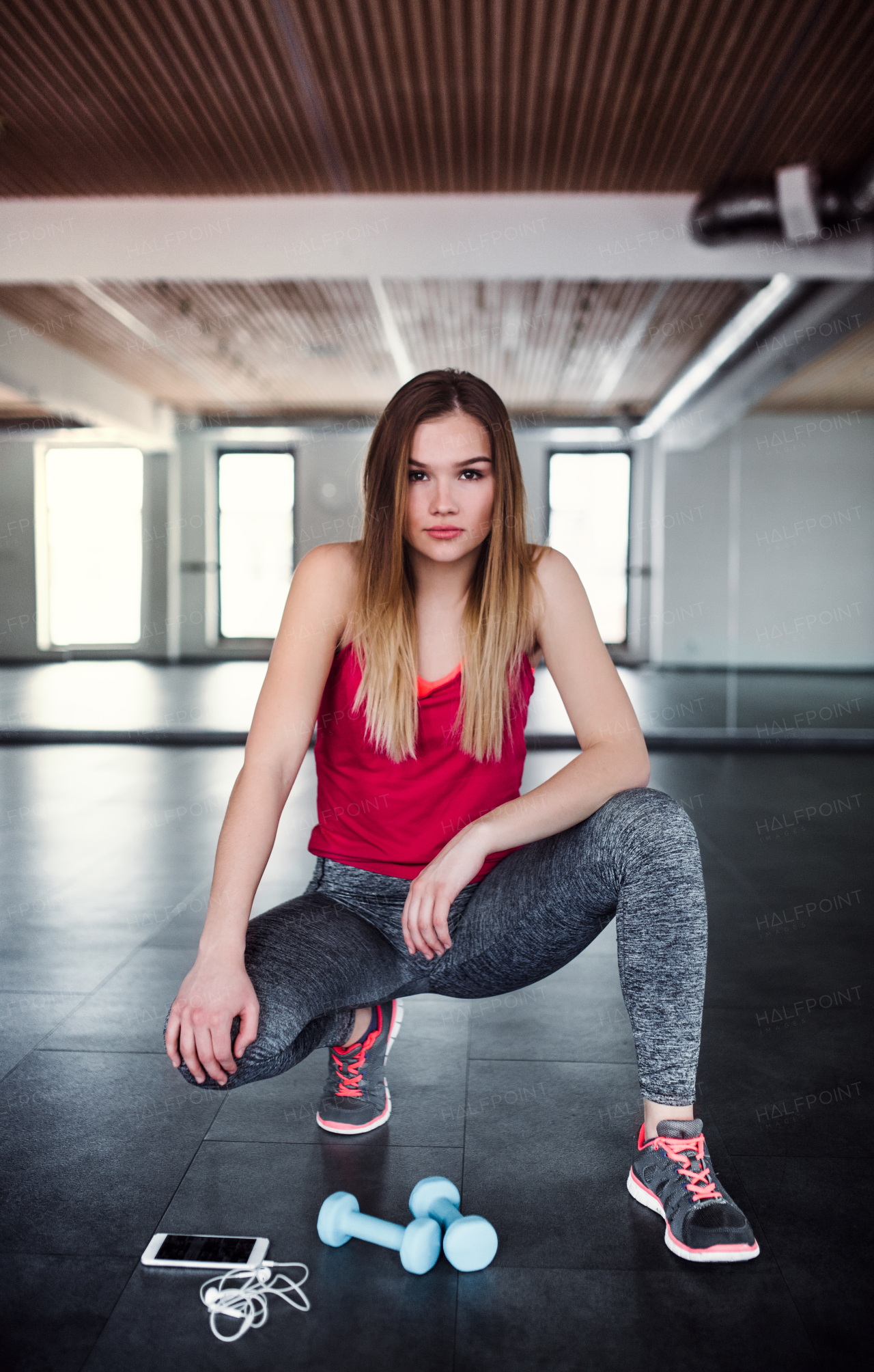 A portrait of a beautiful young girl or woman with dumbbells and smartphone in a gym.