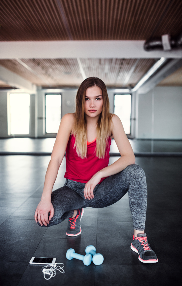 A portrait of a beautiful young girl or woman with dumbbells and smartphone in a gym.