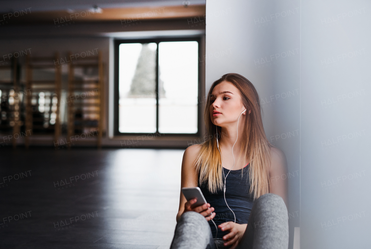 A young girl or woman with earphones and smartphone in a gym, listening to music. Copy space.