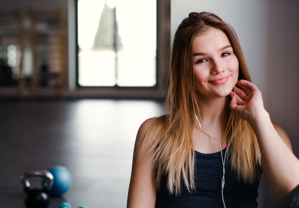 A young girl or woman with earphones and smartphone in a gym, listening to music. Copy space.