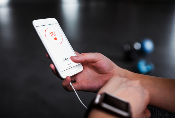 A midsection of woman with smartwatch and smartphone in a gym, checking heart rate.