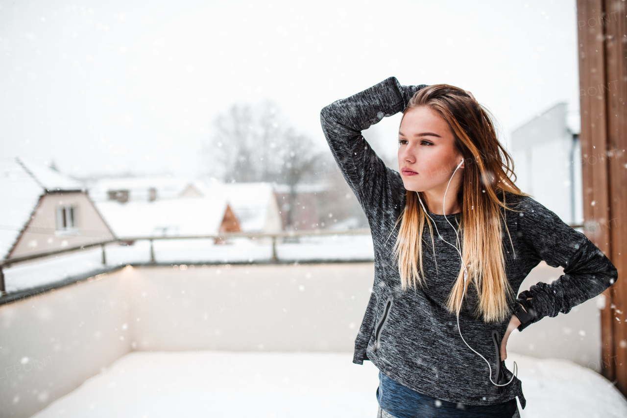 A portrait of young girl or woman with earphones doing stretching outdoors on a terrace in winter. Copy space.