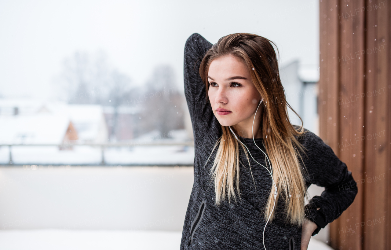 A portrait of young girl or woman with earphones doing stretching outdoors on a terrace. Copy space.