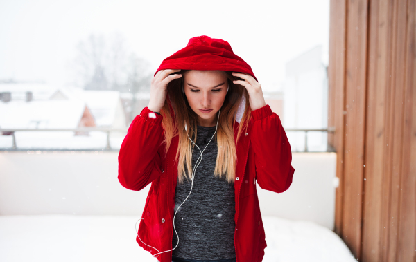 A portrait of beautiful young girl or woman with earphones outdoors, listening to music.