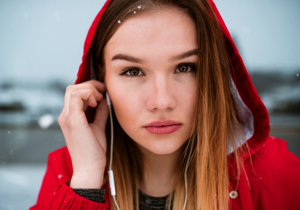 A close-up portrait of beautiful young girl or woman with earphones outdoors, listening to music.