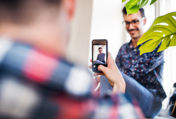 Two young friends with smartphone sitting indoors, taking photos. House sharing concept.